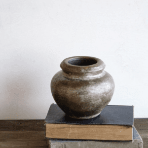 A rustic clay pot placed on two stacked vintage books against a plain wall.